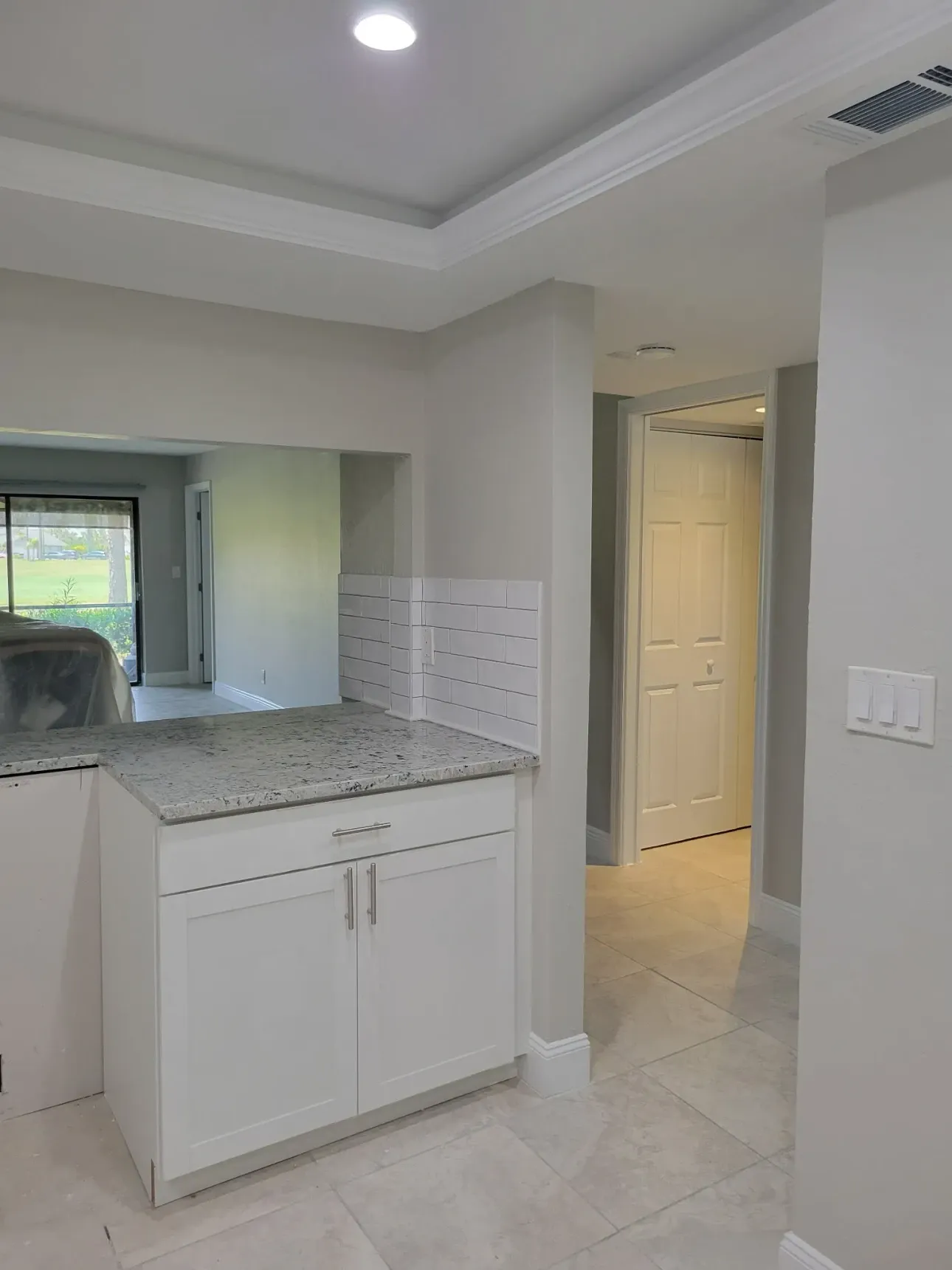 Granite-topped peninsula with a subway tile knee wall opening to a hallway and lanai view, tray ceiling and continuous tile floor